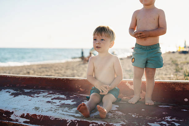 Twin brothers are enjoying a relaxing day at the beach, sitting on an old boat and playing