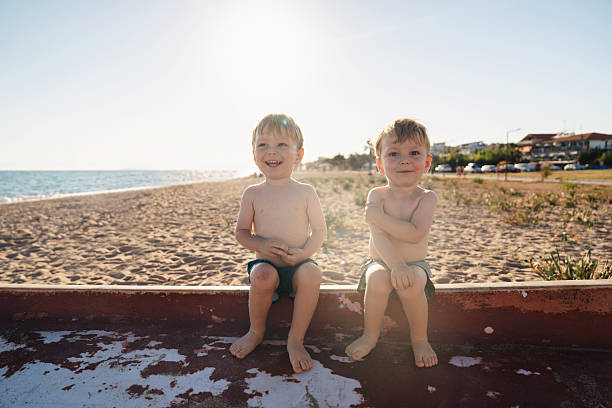 Twin brothers are enjoying a relaxing day at the beach, sitting on an old boat and playing