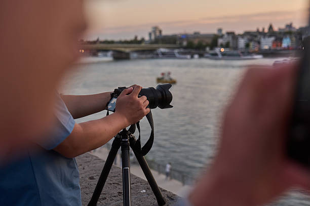 Adult photographer using a mirrorless camera on a tripod shooting a city river view at dusk