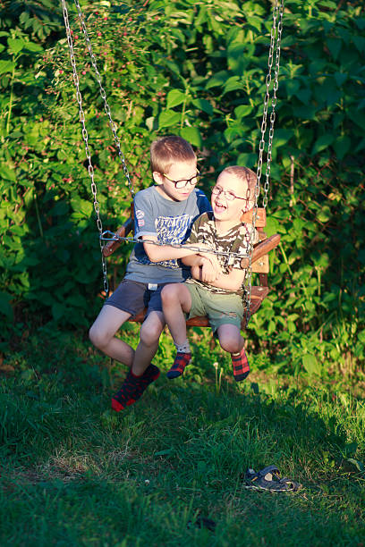 Two boys playing together on a swing, enjoying vacation time outdoors.