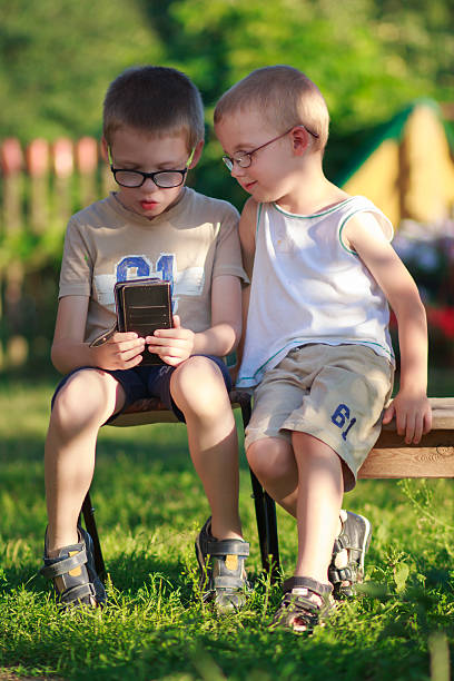 Young siblings enjoying summer vacation together outdoors, sharing fun with a smartphone.