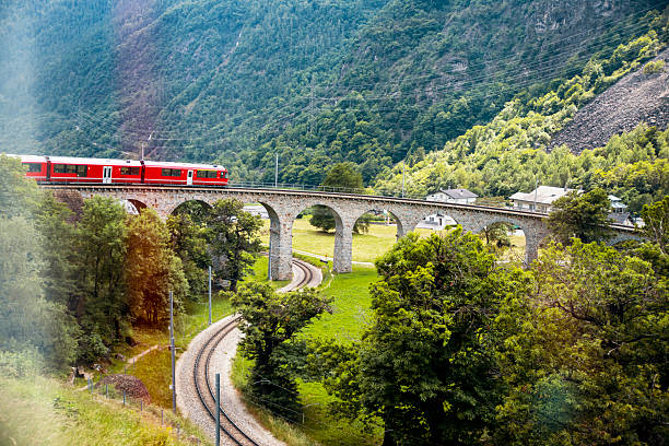 Red Swiss train passes bridge in green mountain valley in European Alps