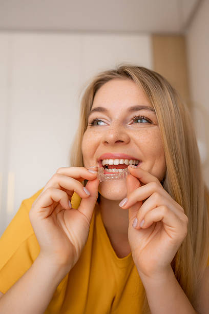 istock Woman smiling while inserting clear dental aligner into her mouth 2236490488