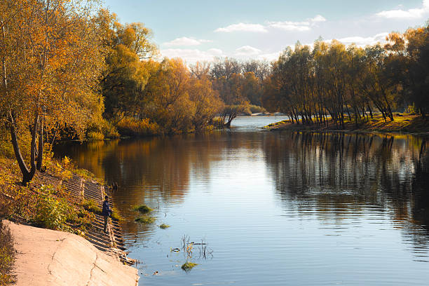 Tranquil autumn landscape with a calm river surrounded by golden trees, clear reflections in the water, and warm sunlight. The peaceful natural scenery is ideal for themes related to nature, relaxation, travel, and seasonal backgrounds.