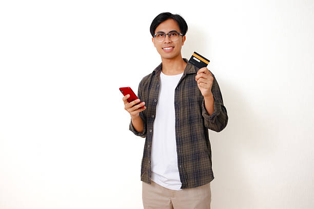 istock Smiling young Asian man holding a product card while using his phone on a white background 2236500046