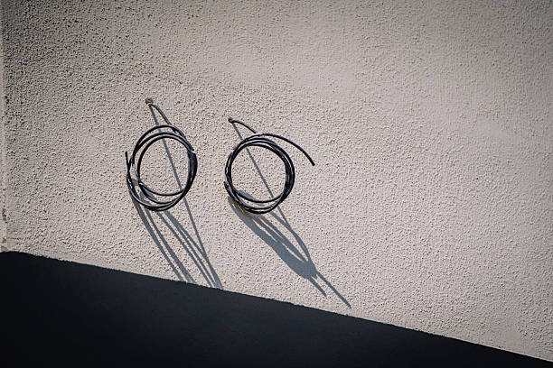istock Two coiled black cables mounted on a textured beige wall with strong sunlight casting long shadows, creating a minimal and abstract composition. 2236510377