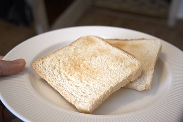 Freshly toasted bread slices served on a white plate with hand  in soft morning light.