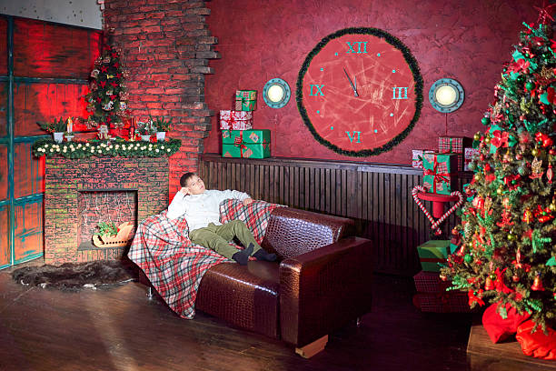 A cheerful elementary age boy dressed in casual clothes is waiting Christmas while sitting on the couch. The traditional red and green colors in Christmas decor of the living room. Studio shooting