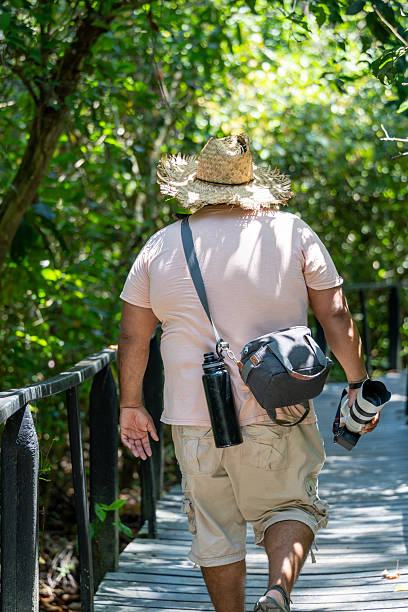istock Man hiking a tropical jungle boardwalk, carrying camera and wearing a straw hat 2236525042