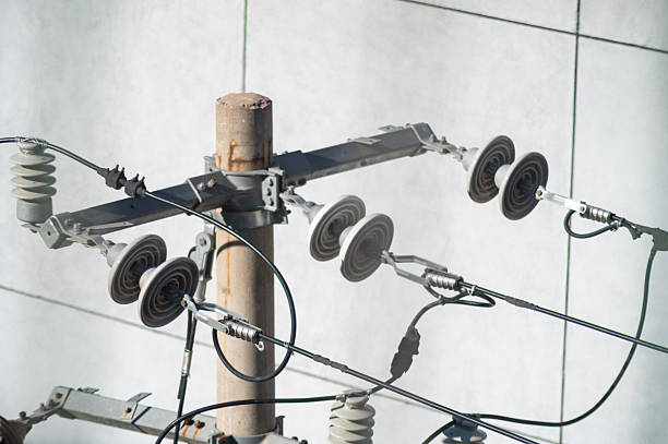 Concrete utility pole with attached power lines, insulators, and electrical cables against a plain background