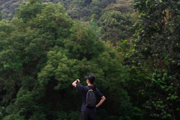 istock Back view of a woman with a backpack looking at her watch while standing in front of a dense green forest. 2236525793