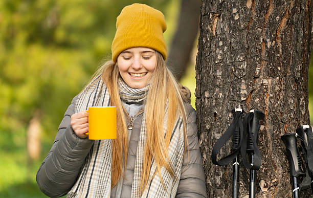 istock Hiker drinking hot beverage from yellow mug leaning against tree 2236533161