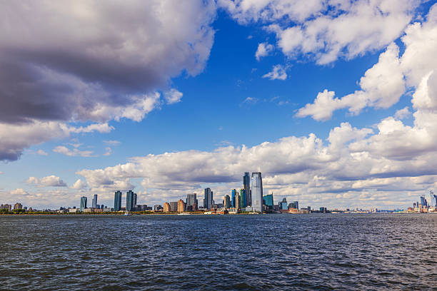 Hudson River with modern Jersey City skyline on background and dramatic cloudy blue sky. New York. USA.