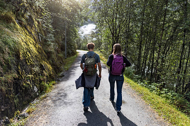 Young girl personal trainer walking with an old man through a path in suburban area.