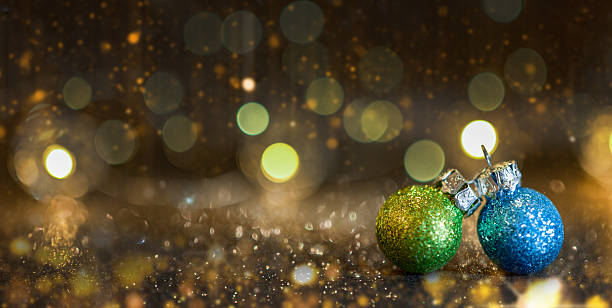 Close-up of green and blue glitter Christmas ornaments on a sparkling surface with golden bokeh lights in the background. Festive holiday concept for Christmas, New Year, celebrations, and winter decoration.