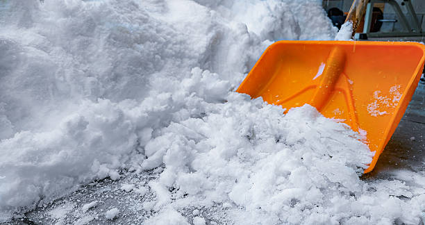 Close-up of an orange plastic snow shovel partially buried in fresh snow. Perfect for concepts of winter season, snow removal, outdoor work, tools, manual labor, and cold weather challenges.