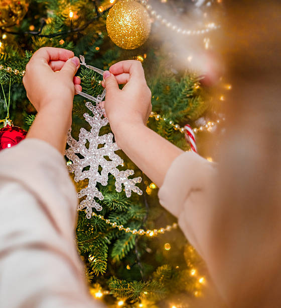 Close-up of hands hanging a sparkling snowflake ornament on a Christmas tree decorated with baubles and lights. Festive holiday concept, family tradition, winter celebration, and joyful seasonal atmosphere.
