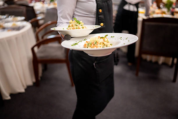 istock Waiter serving gourmet dishes in upscale restaurant. Elegant dining atmosphere with white tablecloths, wooden chairs, and active service 2236543250