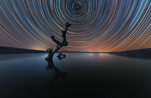 istock Star Trails Over Dead Tree Reflecting on Still Water 2236545096