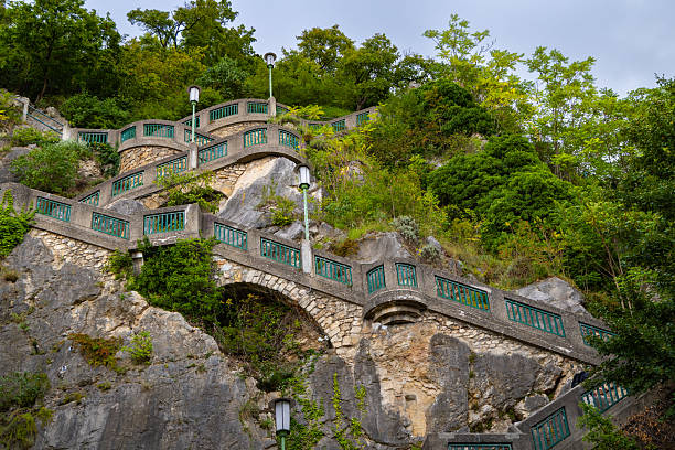Stone staircase with green railings winding up the rocky hillside surrounded by lush greenery. Picturesque architectural detail, perfect for travel, tourism, history, and exploration concepts.
