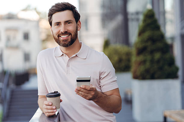 istock Smiling man holding smartphone and coffee in city 2236552778