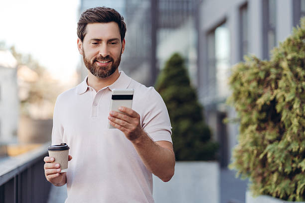 Bearded man using smartphone and drinking coffee in city