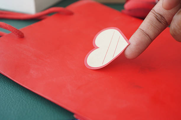 A finger gently places a heart note on a vibrant red gift bag.