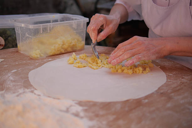 Hands roll out dough while preparing fresh ingredients at a kitchen table.