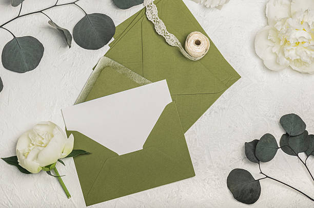 istock Feminine invitation or greeting card mockup with green envelope, gift box and white peony flowers, eucalyptus sprigs and openwork ribbon on light background. Blank postcard. 2236572755