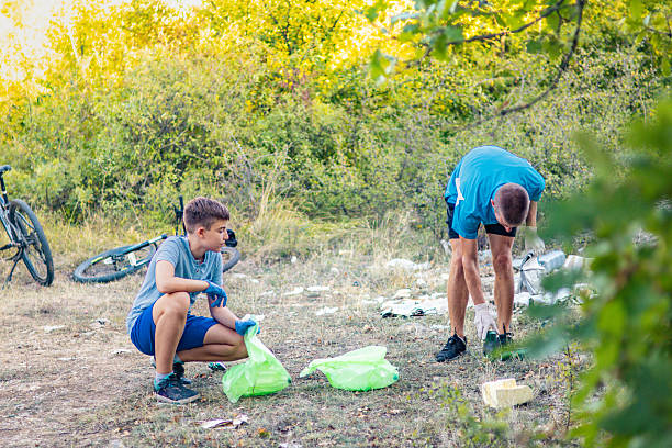 istock Father and son picking up trash during their weekend bicycle ride in nature. Keeping the environment clean, collecting plastic bottles, cans and other garbage in recycling bags, while riding electric bikes as a sustainability concept. 2236574174