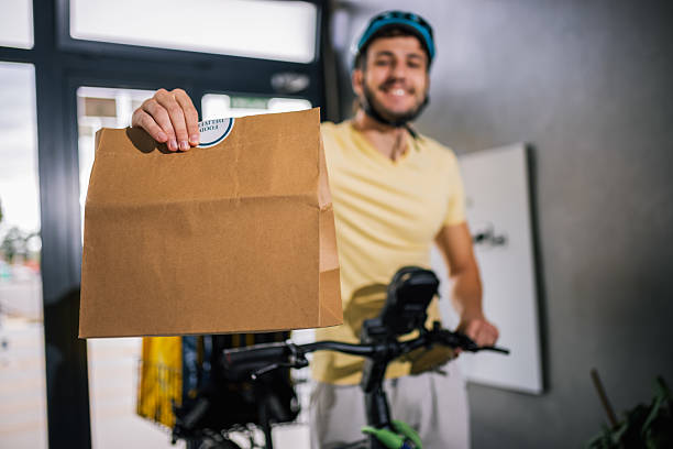 istock Courier with bicycle holds food package in hand while entering building, concept of fast delivery, urban service, courier job, modern city lifestyle. 2236582015