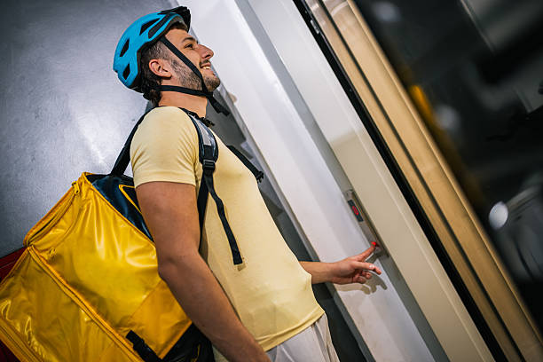 Delivery courier stands with package in front of elevator, concept of transport, logistics, courier job, modern city lifestyle, fast service.