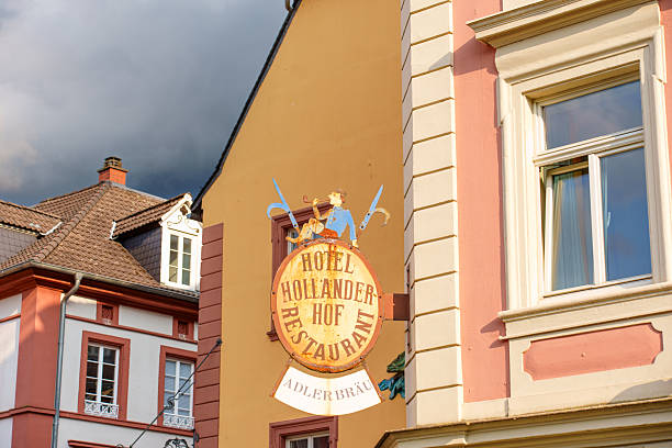 Heidelberg, Germany - June 8, 2025: Colorful sign of Hotel Hollaender Hof Restaurant hanging among historic buildings in Heidelberg, Germany, featuring characters with swords under a dramatic sky.