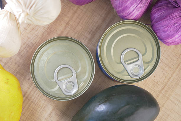 Cans of food placed near fresh vegetables and fruits on the table.