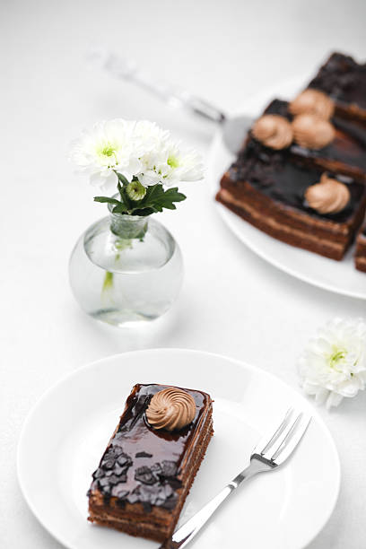 Rich chocolate cake slice with cream swirl on white plate with white flowers and fork