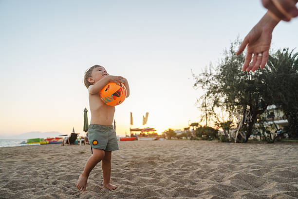 Happy little boy playing with his mom on beach during sunset