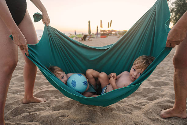 Two young boys relaxing in a makeshift hammock on a sandy beach