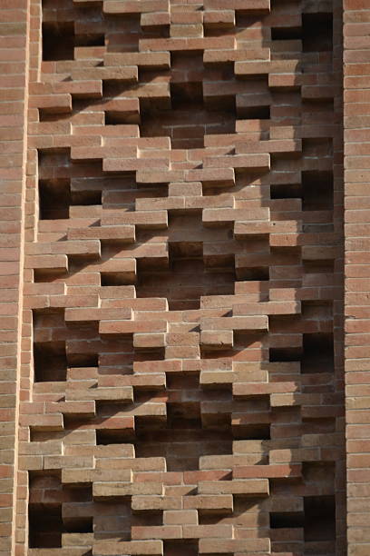 A detailed, eye-level shot captures a brick wall with an intricate, geometric pattern. The reddish-brown bricks are arranged to create a three-dimensional, repeating design, casting strong shadows in the sunlight.