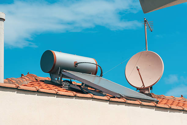 istock Rooftop solar water heater and satellite dish installed on terracotta tiles under clear blue sky. Eco-friendly renewable energy system on residential building in sunny climate. 2236606779