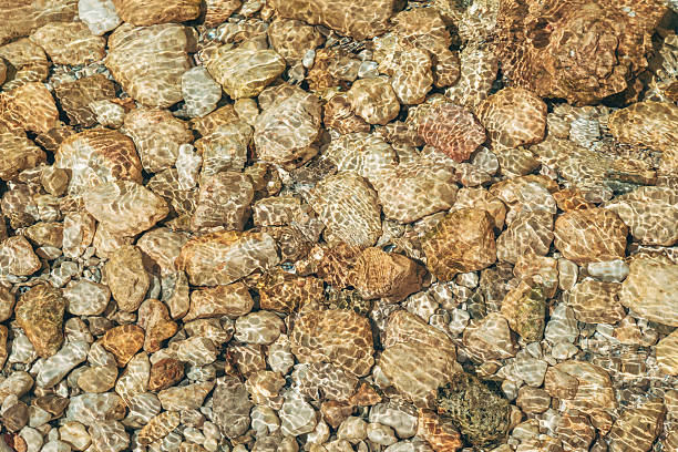 istock Rocks at the bottom of a mountain creek with sunlight caustic effect on clear water surface. 2236608174