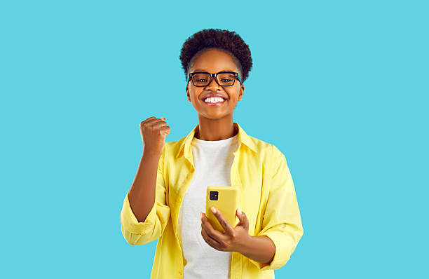 Excited african lady with smart phone won big prize at online casino. Accountant received news about successfully submitted reports. Communication with office from vacation.