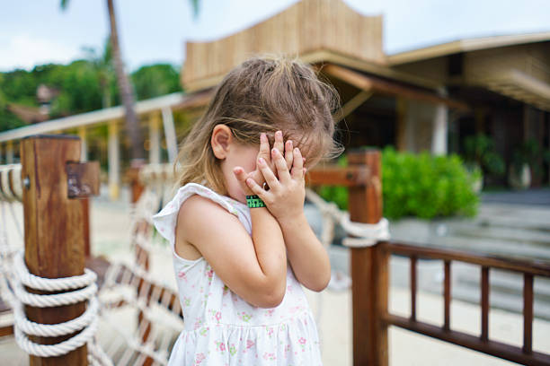 Toddler girl playing a game, covering her face with hands in a tropical resort.
