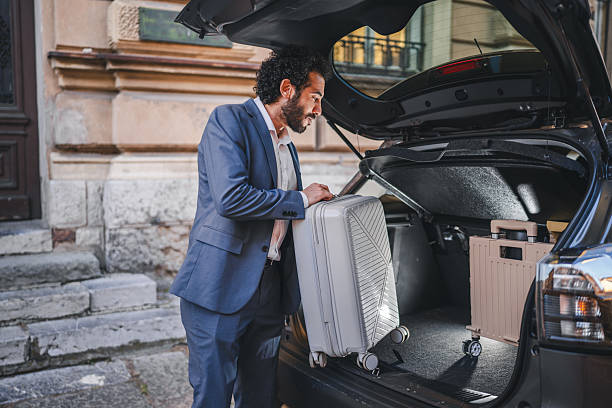 Businessman carefully placing his suitcase into the trunk of a car, preparing for an upcoming business trip, demonstrating the blend of work and travel