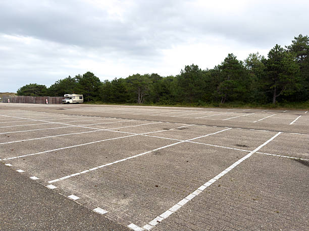 istock Expansive empty parking lot with marked spaces, surrounded by lush greenery and overcast sky, ideal for outdoor activities and events 2236621762
