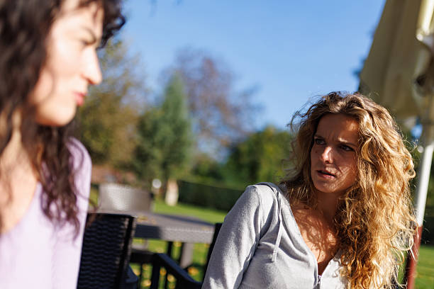 Two women engaged in a serious conversation outdoors on a sunny day in a park, surrounded by nature during late afternoon