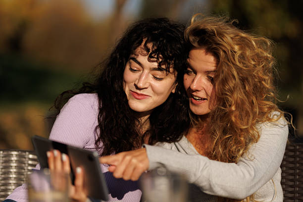 istock Two friends enjoying a sunny day together while sharing a digital device outdoors on a cozy terrace in the late afternoon 2236625374