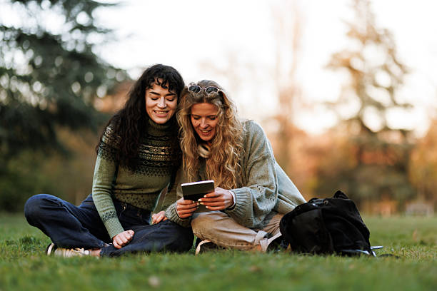 istock Friends enjoy a warm afternoon sharing a moment in the park while looking at a device surrounded by nature and golden light during sunset 2236625436