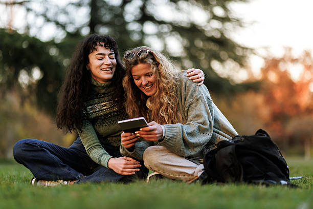 istock Two friends enjoy a relaxed moment outdoors while sharing a tablet during sunset in a serene park, capturing tranquility and joy in nature 2236625440