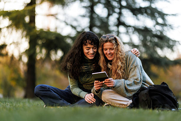 istock Friends enjoying quality time outdoors, engaged with a device in a lush park during a sunny afternoon 2236625444