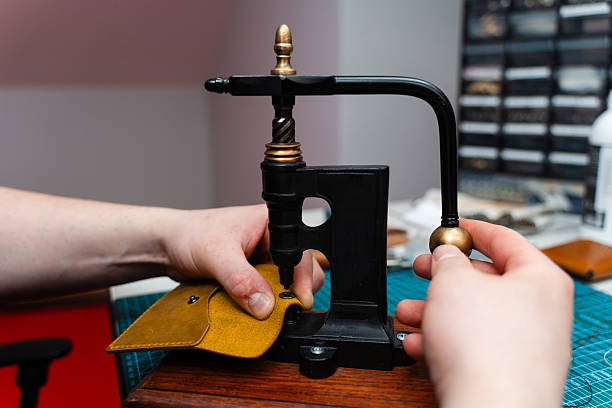 istock Craftsman uses retro rivet press machine to set metal snap button into yellow leather. Leather pressing with a retro rivet machine ensures strong attachments for bags, wallets, and belts. 2236627278
